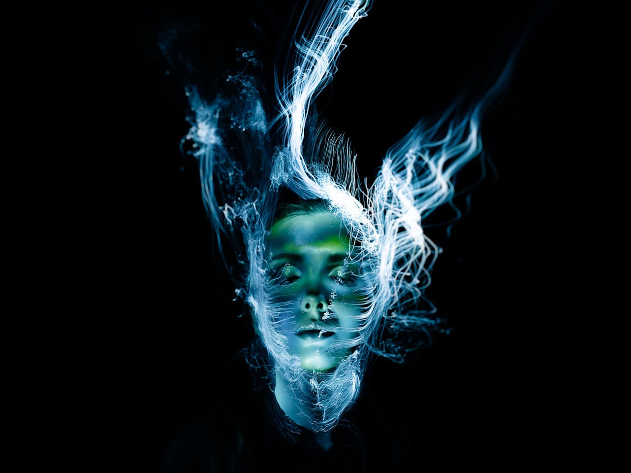 Een kunstzinnige voorstelling van een gezicht met levendige blauwe en groene lichtgolven op een zwarte achtergrond.