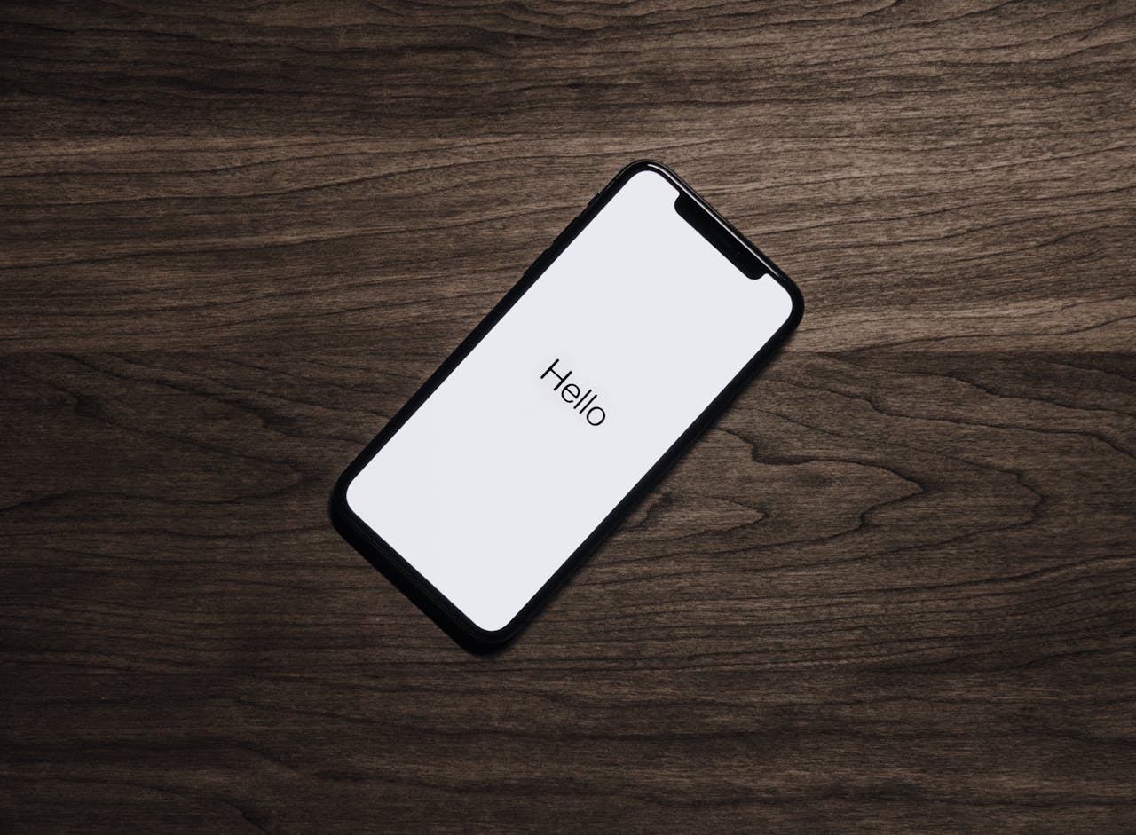 Een smartphone ligt op een houten tafel met het woord 'Hallo' op het scherm.