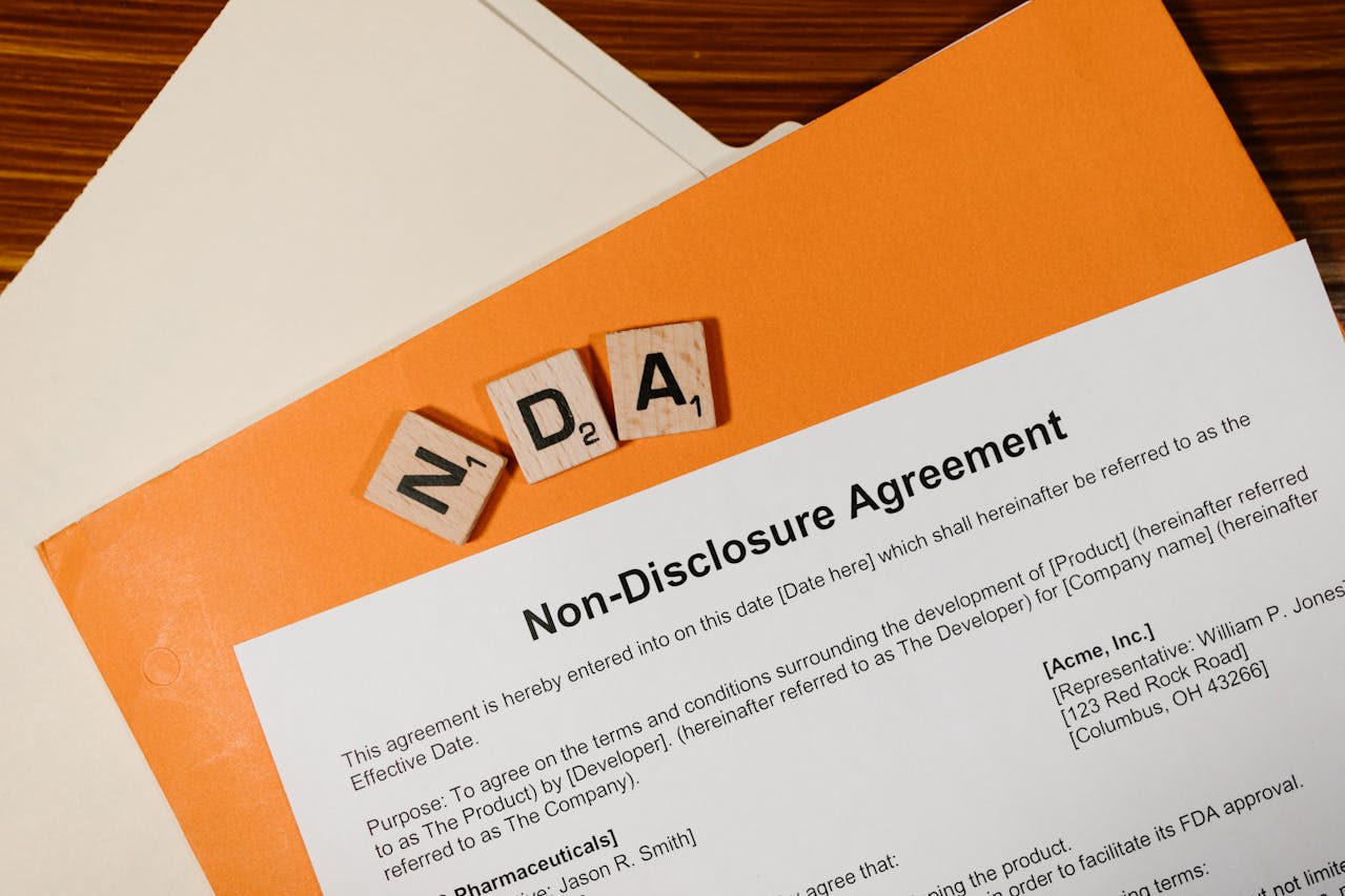 Een close-up van een niet-openbaarmakingsovereenkomst met houten letterblokjes die "NDA" spellen, op een houten tafel.