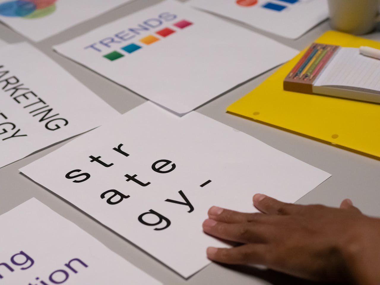 Een hand ligt op een paper met het woord 'strategie', omringd door andere marketinggerelateerde documenten en schrijfmateriaal.