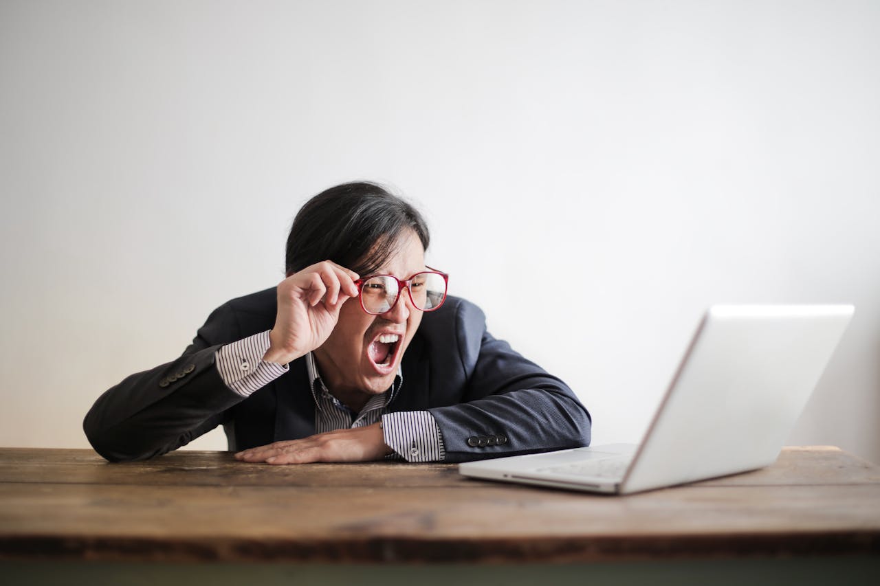 Een man in een blazer roept gefrustreerd terwijl hij naar een laptop kijkt.