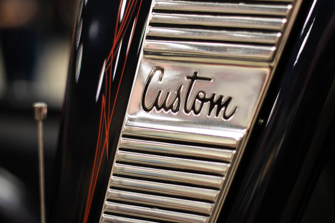 Close-up of a polished chrome emblem labeled "Custom" on a classic vehicle with decorative features.