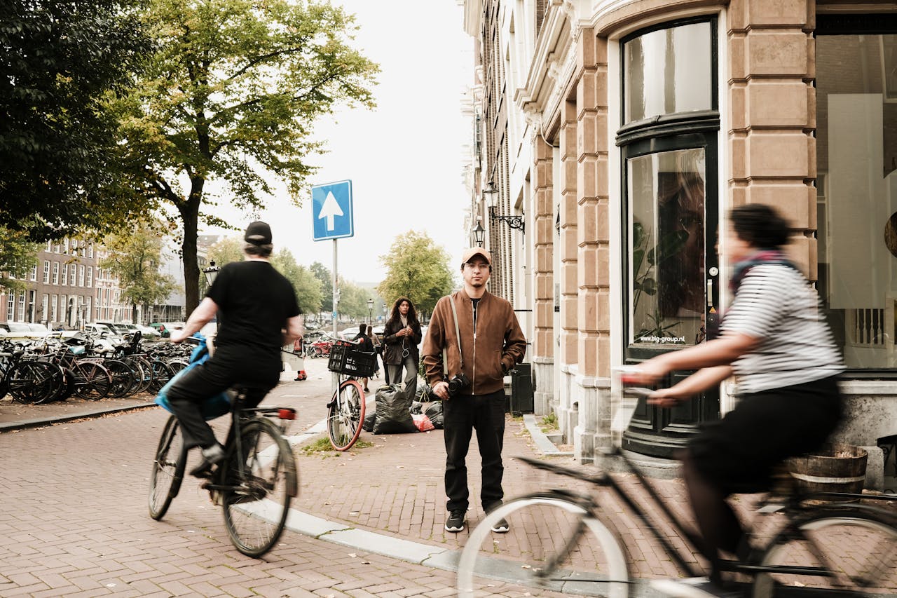 Een jongeman staat op een hoek terwijl fietsers voorbijrijden in een levendige stadsomgeving.