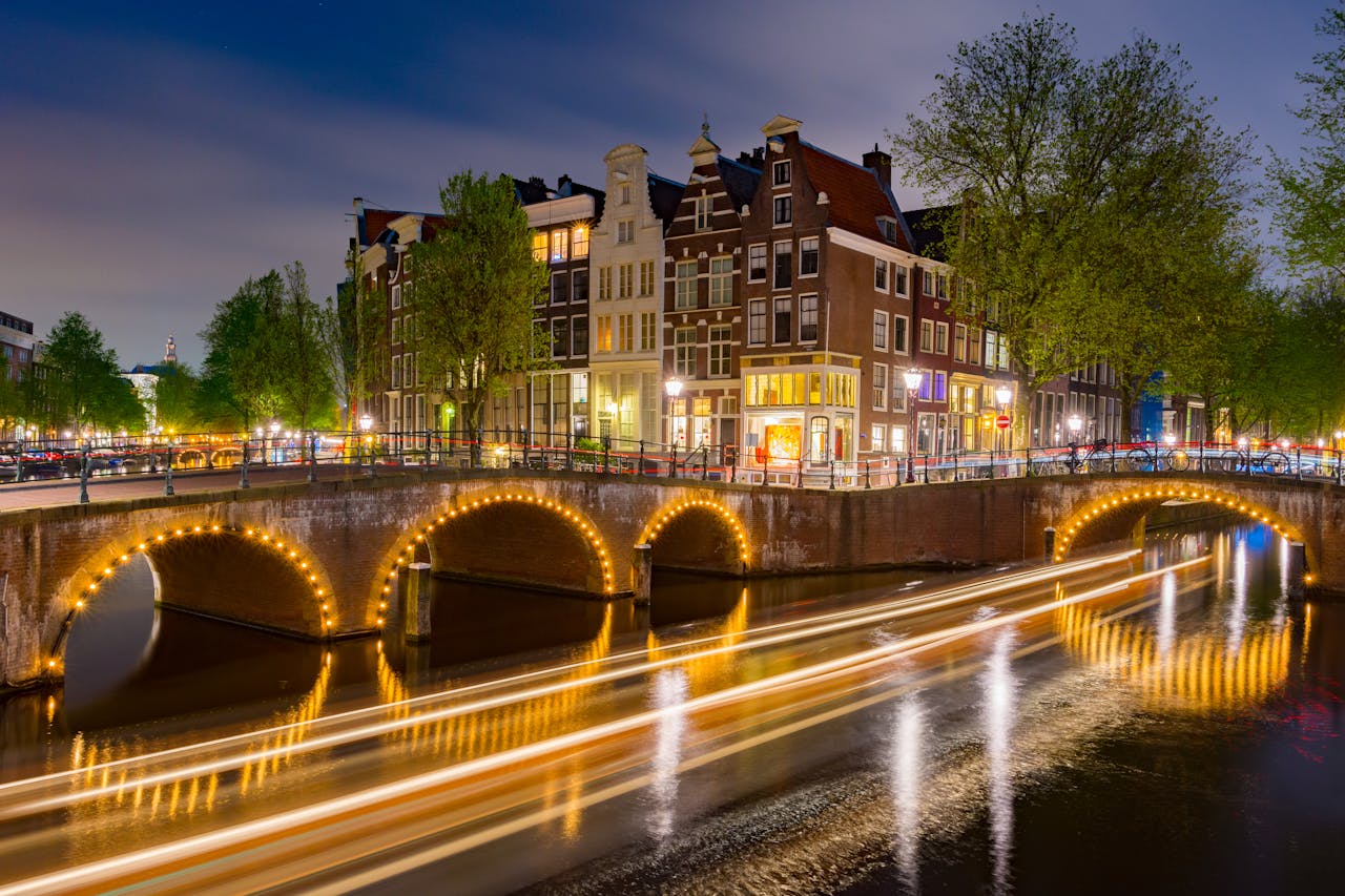 Een pittoreske amsterdamse gracht met verlichte bruggen en een boot die voorbij vaart onder een heldere nachtelijke lucht.